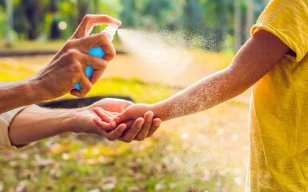 Flacon de répulsif anti-moustique posé sur une table de jardin avec moustique en gros plan sur le bras