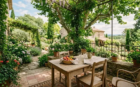 Terrasse ombragée d'un jardin français en été avec une table en bois clair, quelques verres et un panier de fruits, atmosphère paisible d'un après-midi de vacances sans personne visible