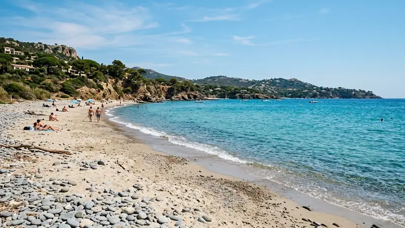 Plage française méditerranéenne en fin de matinée avec sable clair, mer bleu turquoise en second plan et quelques galets au premier plan, ambiance estivale calme sans foule