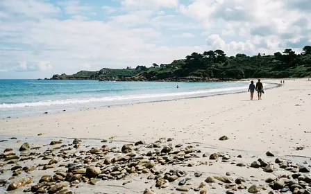 Rivage français en fin de matinée d'été avec sable clair, une petite vague en arrière-plan et quelques galets luisants au premier plan, ambiance de plage calme sans foule