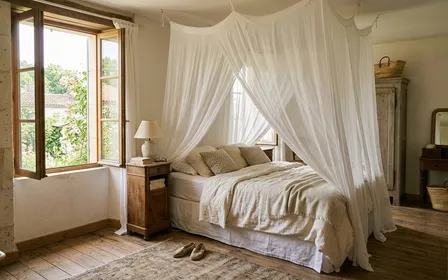 Chambre française sereine avec un lit double couvert d'un voile blanc léger suspendu au plafond en ciel de lit, fenêtre entrouverte laissant entrer la lumière douce de fin d'après-midi d'été