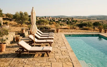 Terrasse française d'été au bord d'une piscine claire avec transats vides et parasol, sol en pierre chauffé par le soleil de fin d'après-midi, ambiance calme et sèche sans végétation luxuriante