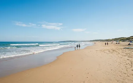 Plage française de sable clair au bord de l'océan Atlantique en été avec vagues douces et ciel dégagé, ambiance calme de matinée ensoleillée sans baigneurs visibles à l'horizon