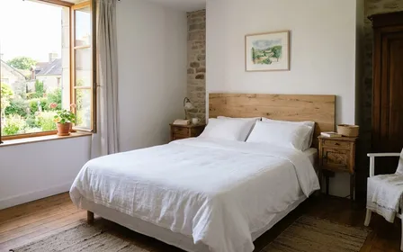 Chambre à coucher française d'été avec draps blancs bien tirés sur un lit double, tête de lit en bois clair et éclairage naturel doux de matinée, ambiance domestique calme et propre