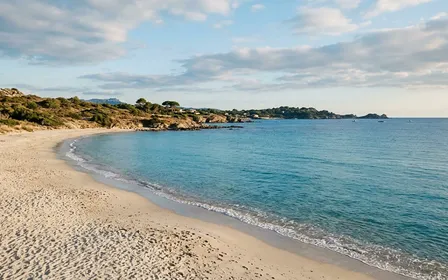 Plage méditerranéenne française déserte en fin d'après-midi d'été avec mer bleue calme et petites vagues, ciel légèrement nuageux et sable clair, ambiance paisible sans baigneur ni méduse visible