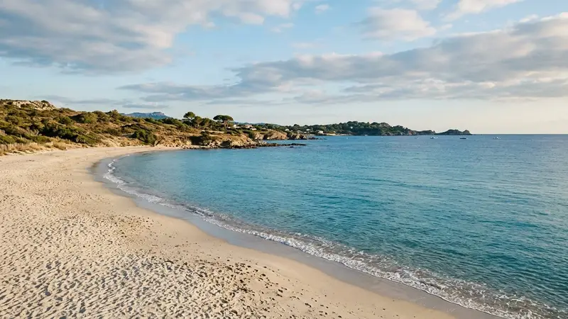 Plage méditerranéenne française déserte en fin d'après-midi d'été avec mer bleue calme et petites vagues, ciel légèrement nuageux et sable clair, ambiance paisible sans baigneur ni méduse visible