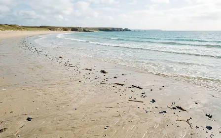 Plage française du littoral atlantique en fin de matinée d'été avec sable clair humide et vagues douces de l'océan, ambiance calme documentaire sans humain visible, quelques débris marins délicats bleutés au bord de l'eau