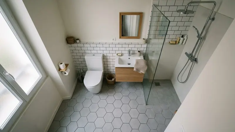 Salle de bain française contemporaine avec cuvette de toilettes fermée en céramique blanche et sol carrelé gris clair vu de dessus, ambiance sobre lumière naturelle douce du matin aucun humain visible plan large documentaire