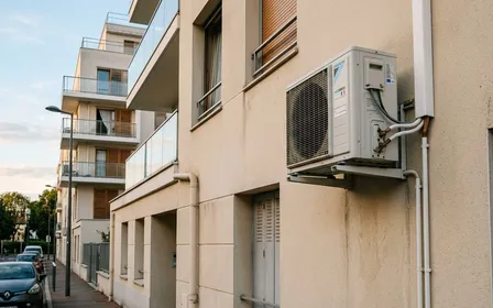 Bloc extérieur de climatiseur français blanc en façade d'immeuble contemporain avec grille de ventilation visible, ambiance sobre lumière naturelle documentaire de fin d'après-midi aucun humain ni animal visible plan rapproché