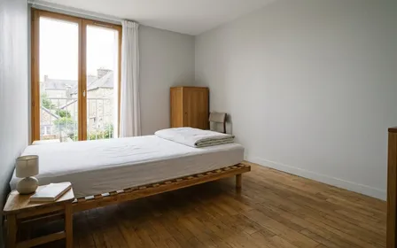 Chambre française d'un logement contemporain avec matelas isolé du mur sur sommier à lattes et housse blanche hermétique tirée jusqu'aux angles, ambiance sobre lumière naturelle documentaire aucun humain visible plan large