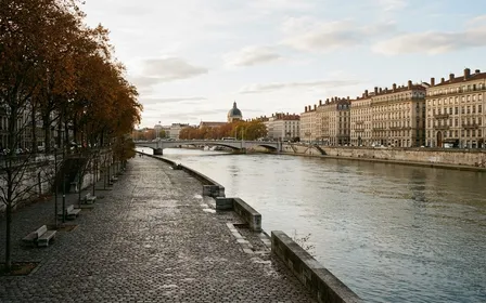Vue générale des quais du Rhône à Lyon en fin d'après-midi d'automne avec berges pavées vides et immeubles haussmanniens lyonnais alignés sur la rive, ambiance sobre lumière naturelle documentaire aucun humain ni animal visible plan large horizontal