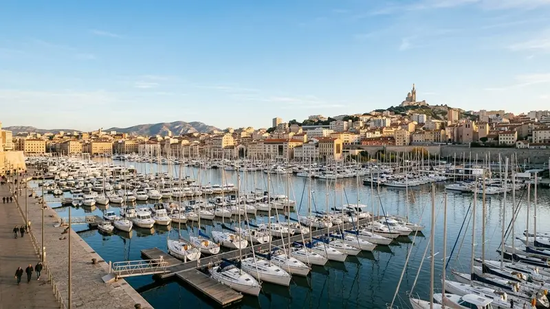 Vue générale du Vieux-Port de Marseille en fin d'après-midi d'automne avec bateaux blancs alignés au premier plan et bâtiments méditerranéens ocre en arrière-plan sous ciel bleu clair, ambiance sobre lumière naturelle documentaire aucun humain visible plan large
