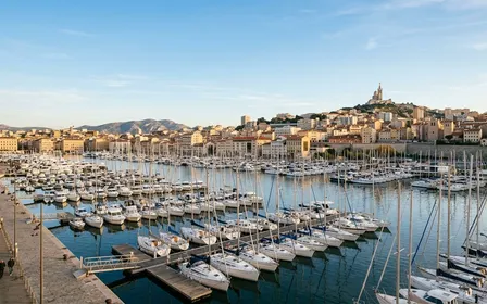 Vue générale du Vieux-Port de Marseille en fin d'après-midi d'automne avec bateaux blancs alignés au premier plan et bâtiments méditerranéens ocre en arrière-plan sous ciel bleu clair, ambiance sobre lumière naturelle documentaire aucun humain visible plan large
