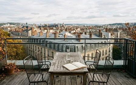 Terrasse extérieure lyonnaise contemporaine avec table en bois et chaises vides en fin d'après-midi d'automne avec vue sur les toits d'immeubles haussmanniens du 2e arrondissement, ambiance sobre lumière naturelle documentaire aucun humain ni insecte visible plan large horizontal