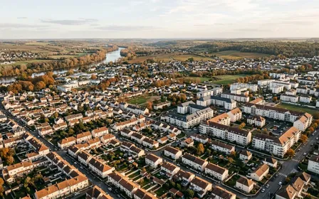 Vue panoramique aérienne d'une région française contemporaine avec toits d'immeubles et pavillons alignés sous ciel dégagé en fin d'après-midi d'automne, ambiance sobre lumière naturelle documentaire aucun humain visible plan large horizontal