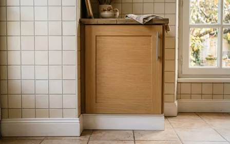 Coin de cuisine française contemporaine en carrelage clair avec plinthes blanches propres et placard bas fermé en début de matinée d'automne, ambiance sobre lumière naturelle documentaire aucun humain ni insecte visible plan macro rapproché horizontal