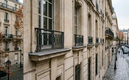 Façade d'immeuble français contemporain haussmannien en pierre claire avec rebord de fenêtre équipé de pointes anti-pigeons métalliques en acier inoxydable en fin d'après-midi d'automne, ambiance sobre lumière naturelle documentaire aucun humain ni oiseau visible plan large horizontal