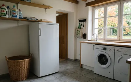 Buanderie française contemporaine avec congélateur blanc armoire fermé et panier à linge vide posé à côté en début d'après-midi d'automne, ambiance sobre lumière naturelle documentaire aucun humain ni insecte visible plan large horizontal