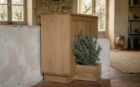 Angle de salon d'une maison française contemporaine avec arrière de buffet en bois clair visible, bouquet de romarin séché noué à la ficelle de jute brute posé contre la plinthe peinte blanche, parquet en chêne ancien, lumière rasante dorée du matin, ambiance patrimoniale sobre, aucun humain ni animal visible, plan serré