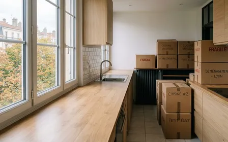 Pièce vide d'un appartement français en cours de déménagement avec plusieurs cartons scellés empilés contre un mur blanc, un vieux grille-pain emballé dans un sac plastique transparent zippé posé sur un carton, un petit piège à phéromones triangulaire en carton beige au premier plan sur le parquet clair, lumière neutre d'après-midi, aucun humain ni animal visible, plan moyen